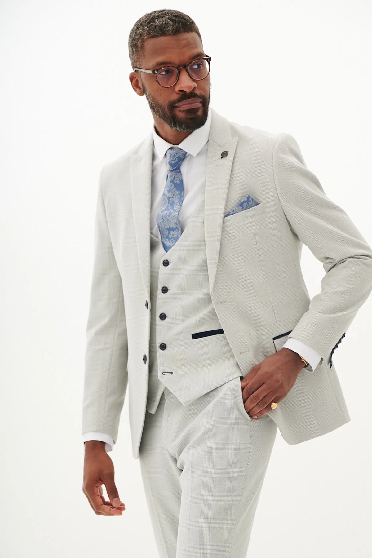 Man wearing a light gray suit with a blue patterned tie and pocket square on a white background.