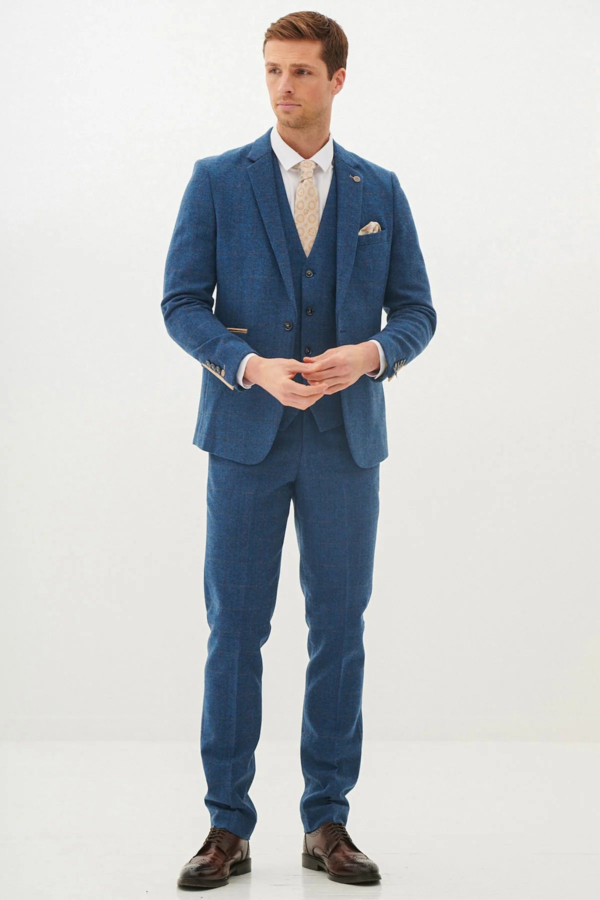 A man wearing a blue tweed check three piece suit with a white shirt and brown shoes.