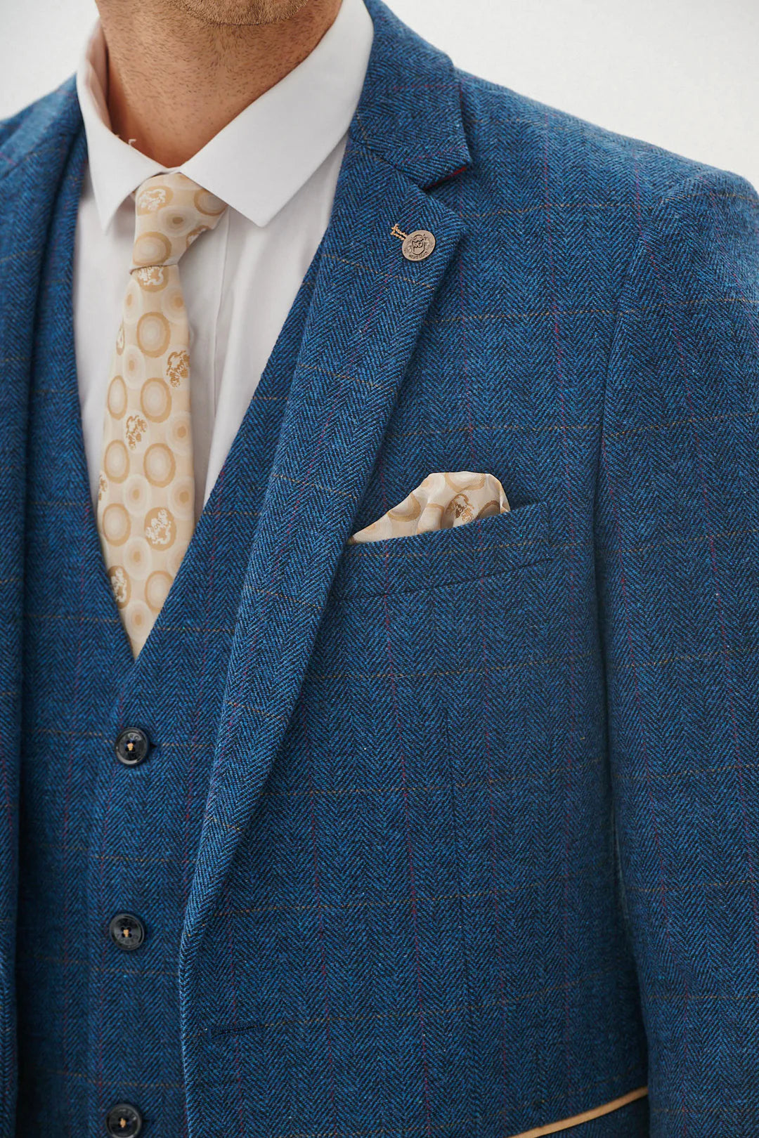 A man wearing a blue tweed check three piece suit with a blue tie and brown shoes.