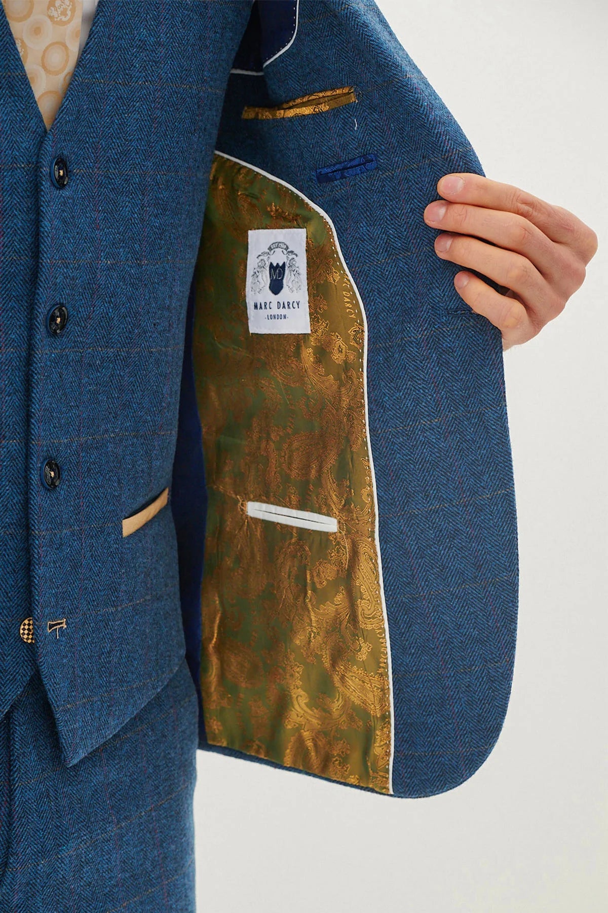 A man wearing a blue tweed check three piece suit with a blue tie and brown shoes.