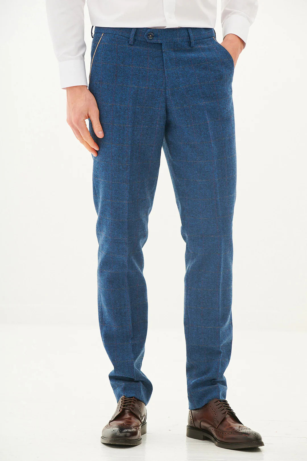 A man wearing a blue tweed check three piece suit with a blue tie and brown shoes.