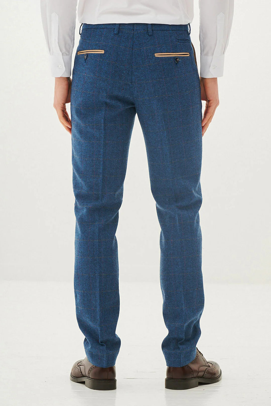 A man wearing a blue tweed check three piece suit with a blue tie and brown shoes.