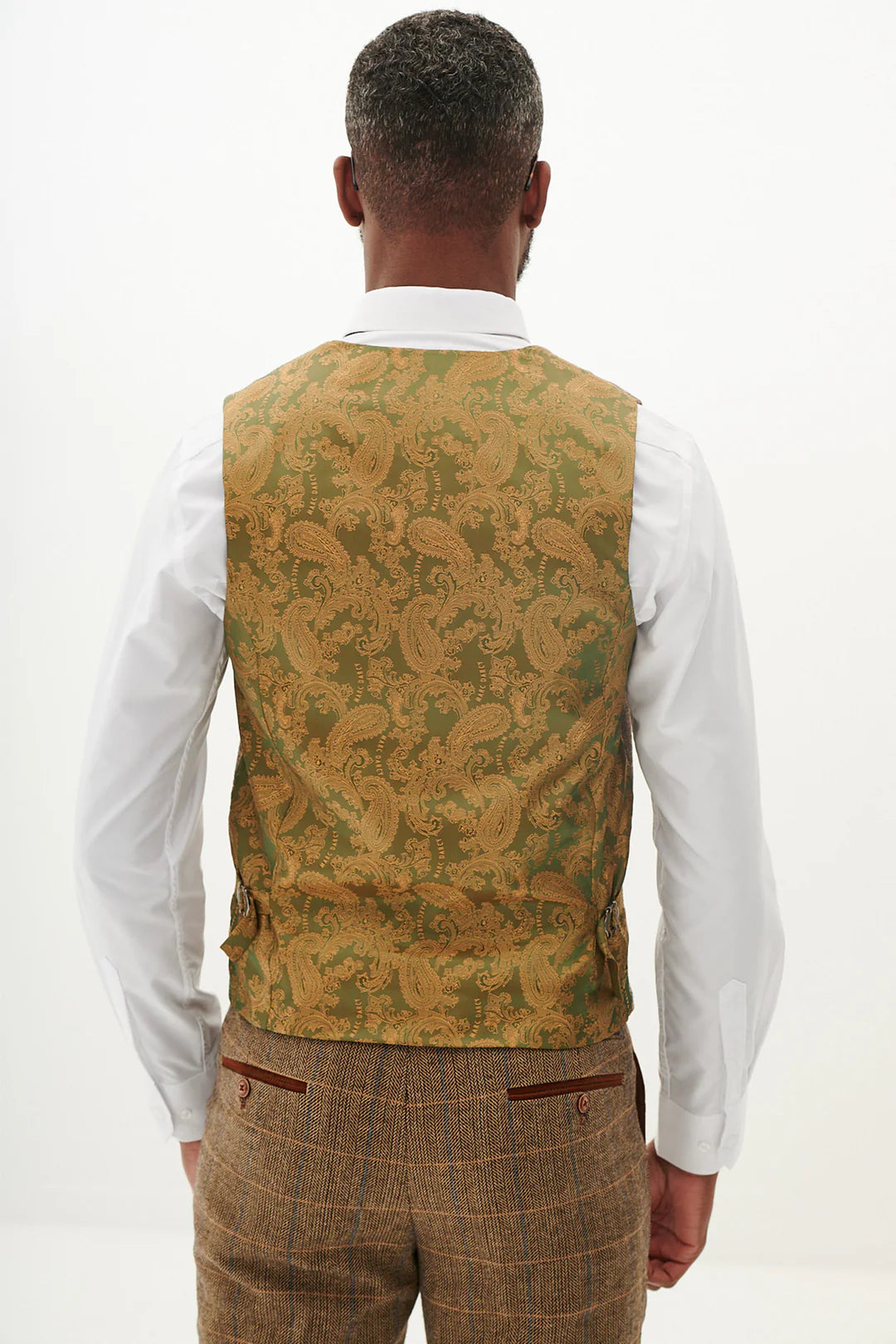 A man wearing a tan tweed check three piece suit with a blue tie and brown shoes.