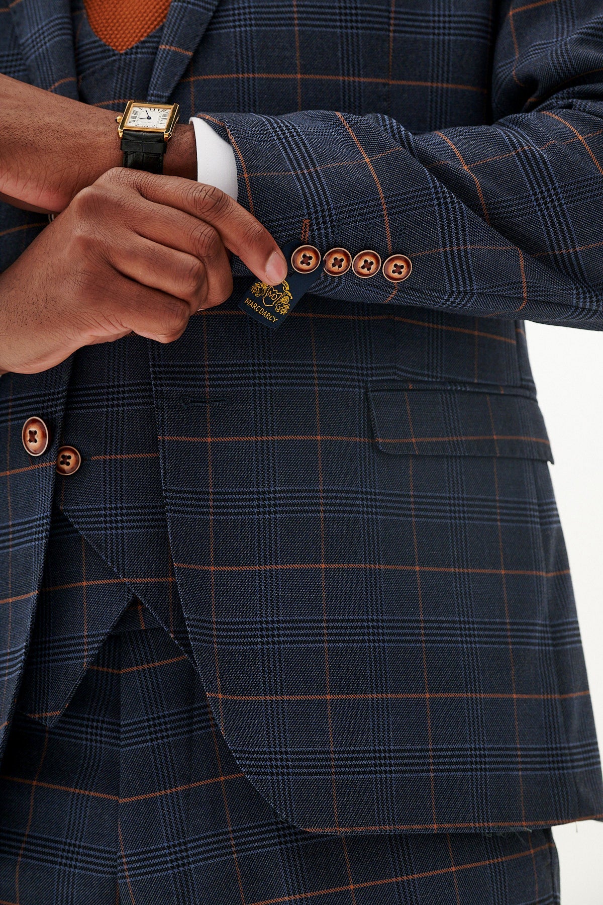 Close-up of a navy blue suit with brown plaid pattern featuring buttons and a hand adjusting it.