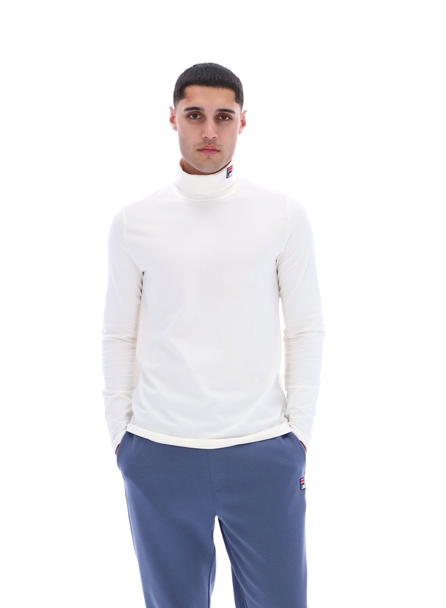 Man wearing a white turtleneck sweater and blue pants on a white background