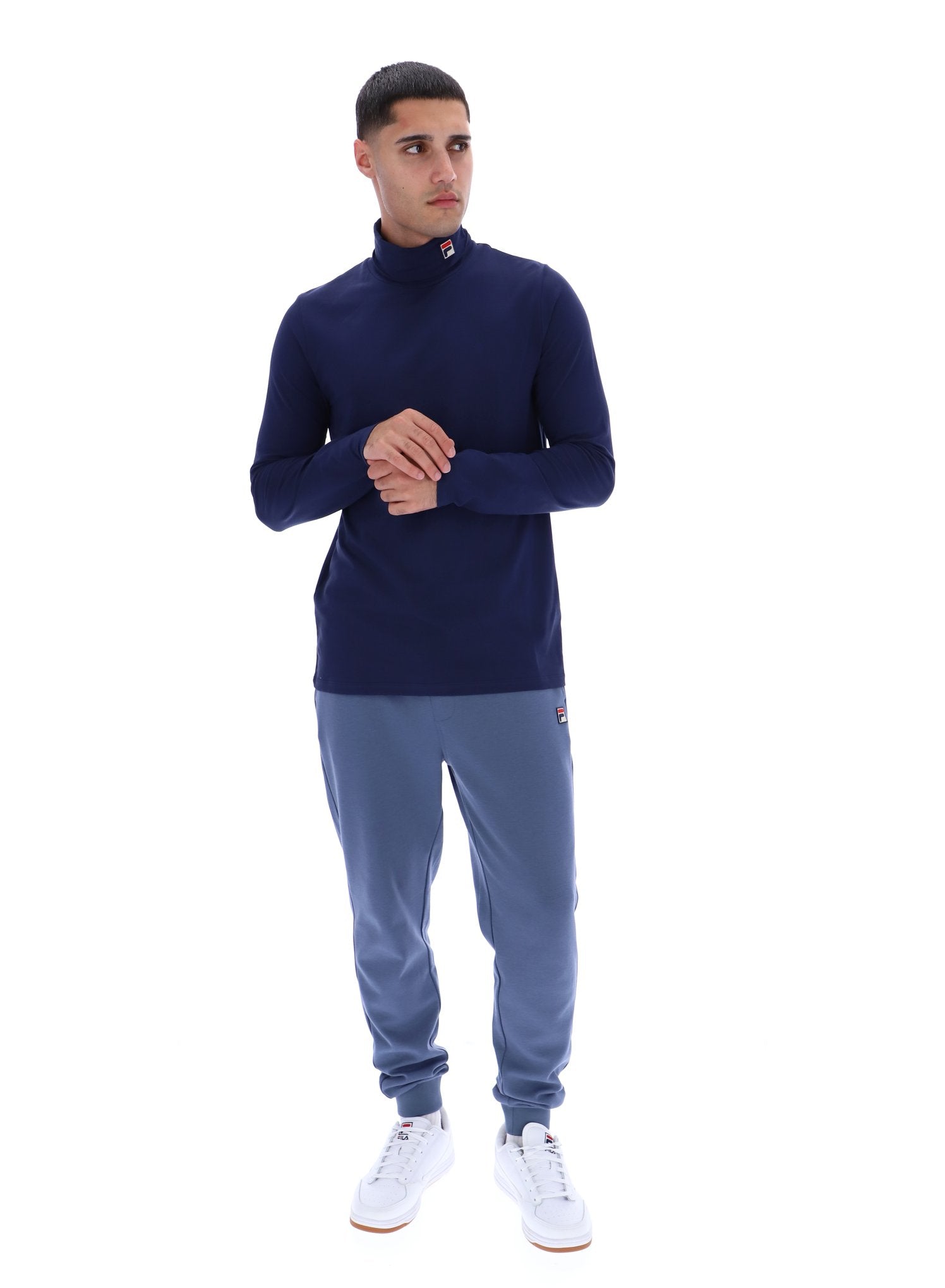 Man wearing a navy turtleneck and gray jogger pants on a white background