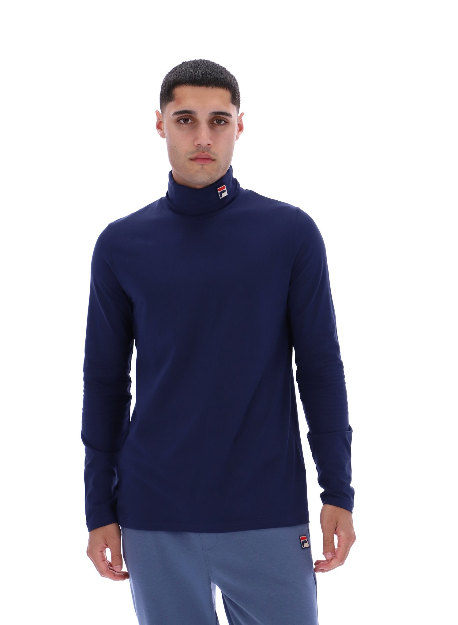 Man wearing a navy blue turtleneck sweater and gray pants on a white background