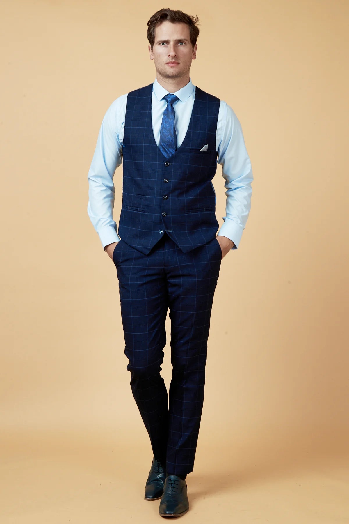 Man wearing a navy suit with a light blue shirt and tie on a beige background.