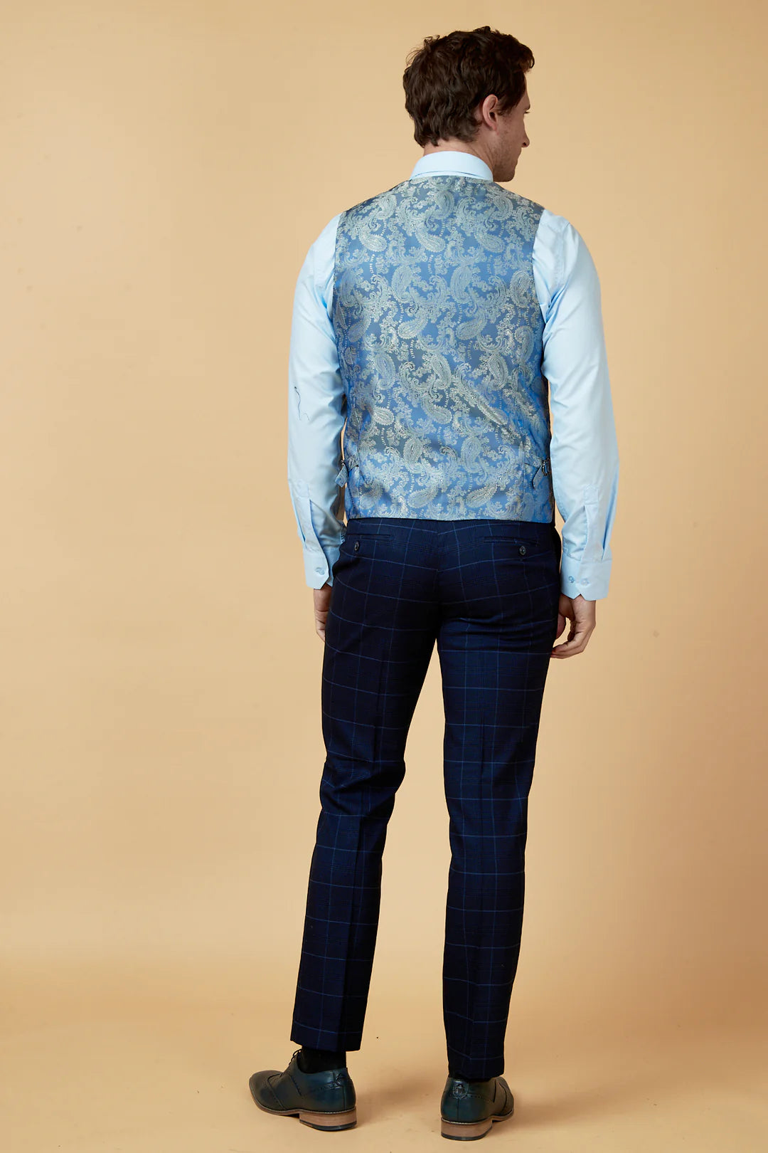 Person wearing a blue patterned vest and dark pants against a beige background