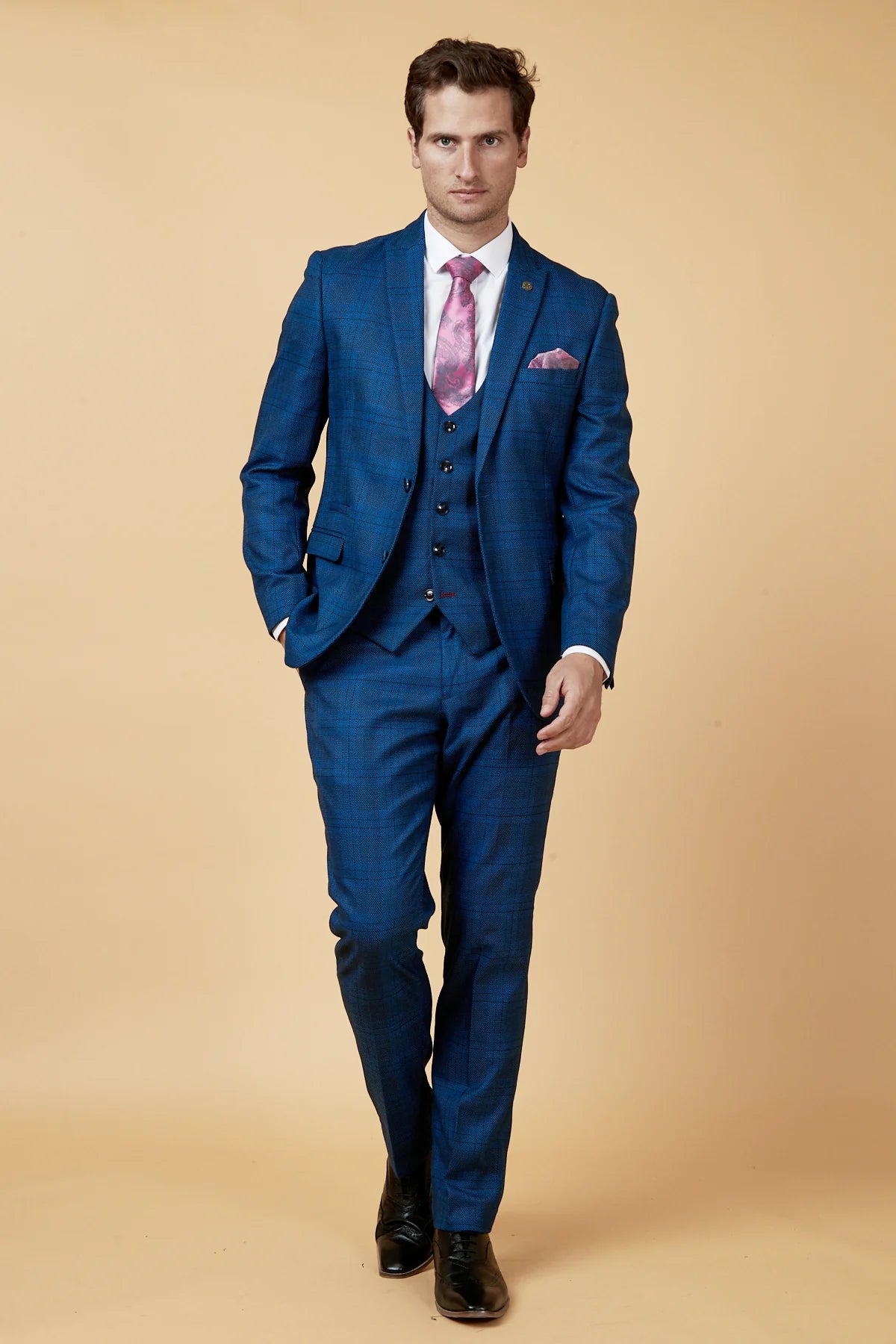 A man wearing a traditional blue with a subtle check pattern suit, featuring a peak lapel, double-breasted design, and a matching pocket square.