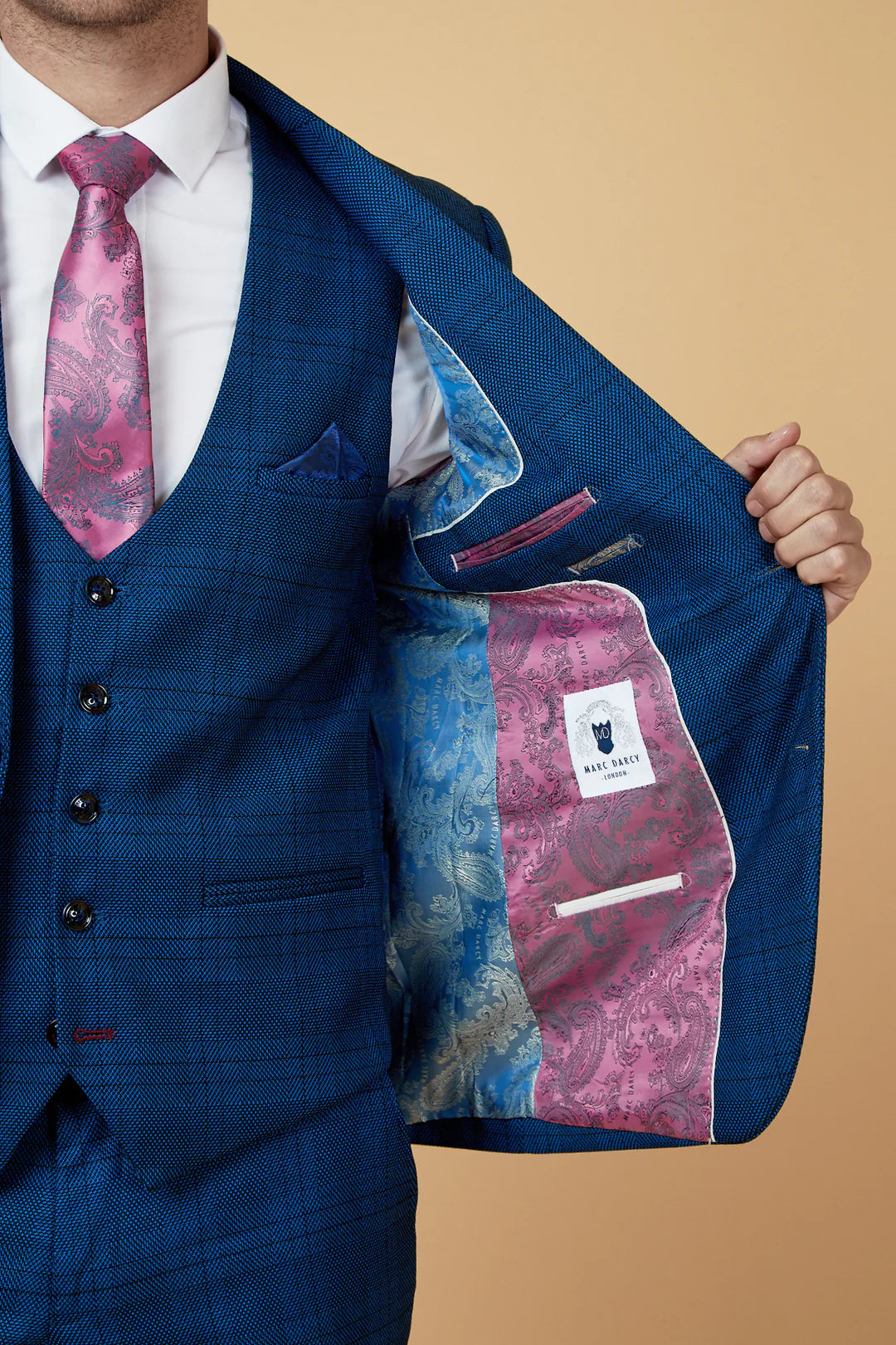 Person wearing a blue suit with a pink and blue patterned tie, holding open a matching jacket against a beige background.