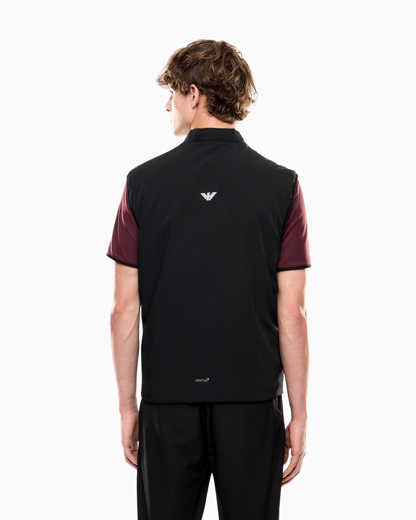 Person wearing a black and maroon polo shirt with a logo on the back, standing against a white background.