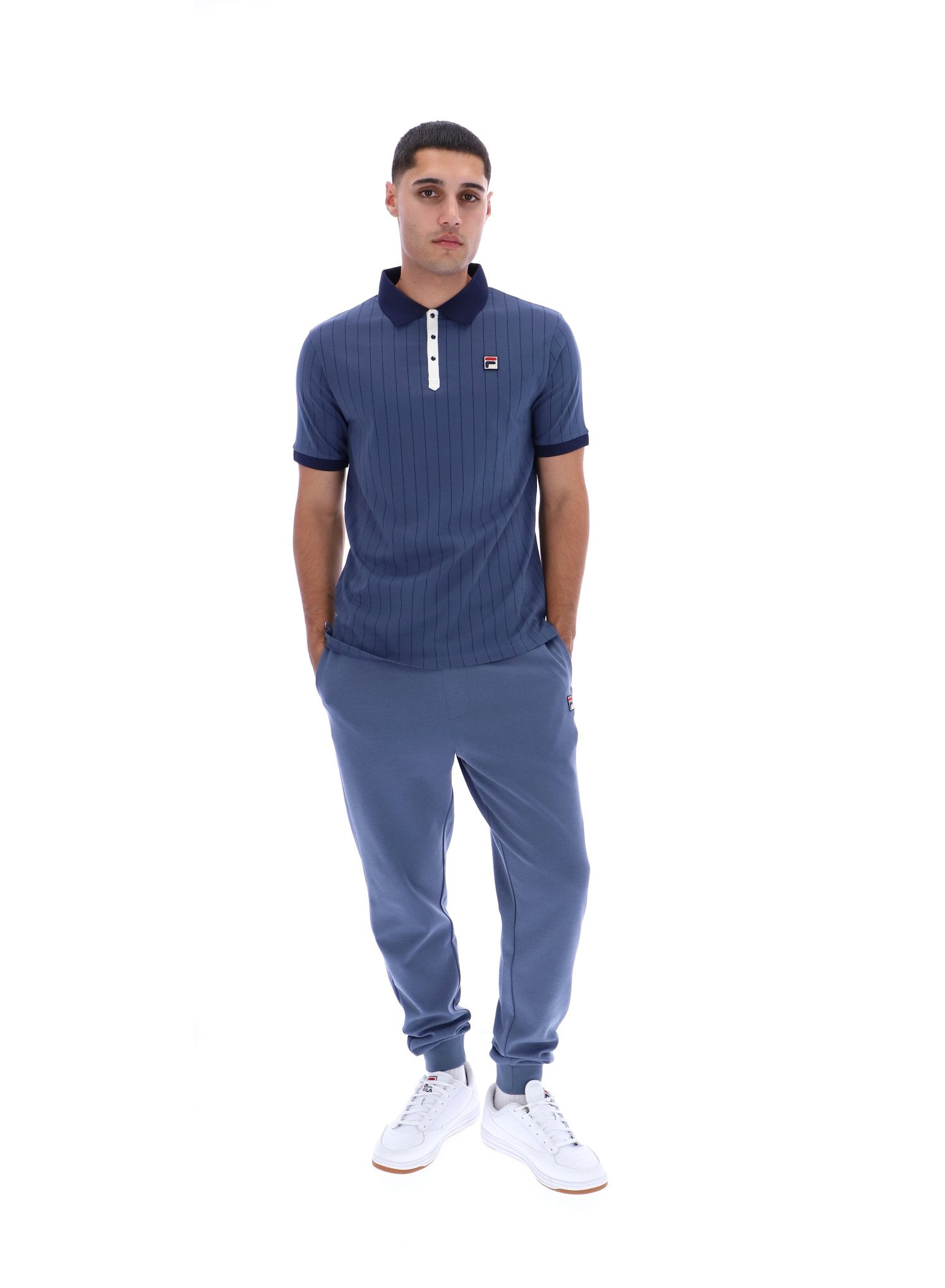 Man wearing a blue ribbed polo shirt and tracksuit on a white background