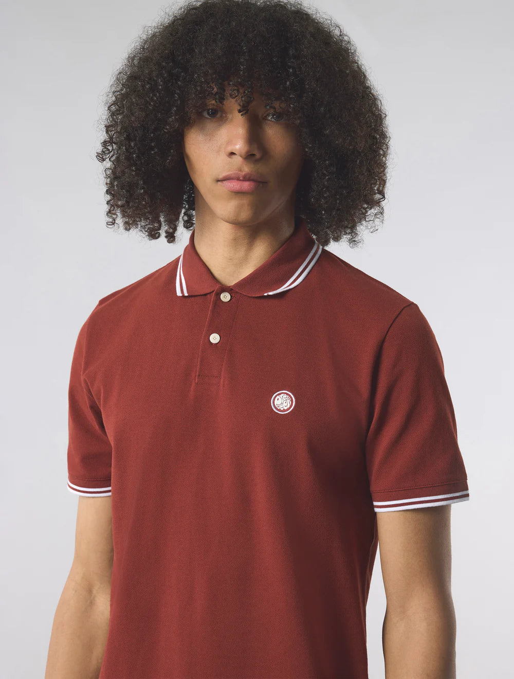 Person wearing a red polo shirt with a small logo on a plain background