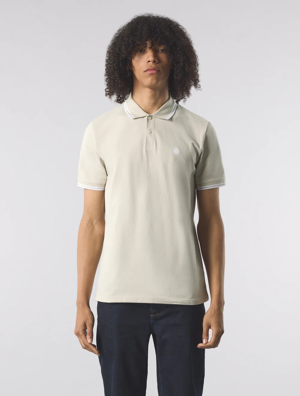 Person wearing a beige polo shirt with a white logo on a plain background