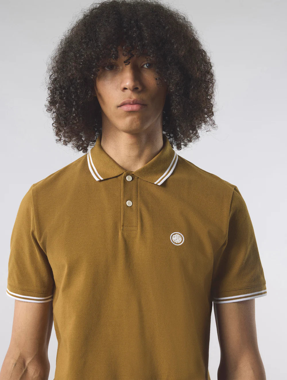 Person wearing a mustard yellow polo shirt with white trim on a plain background