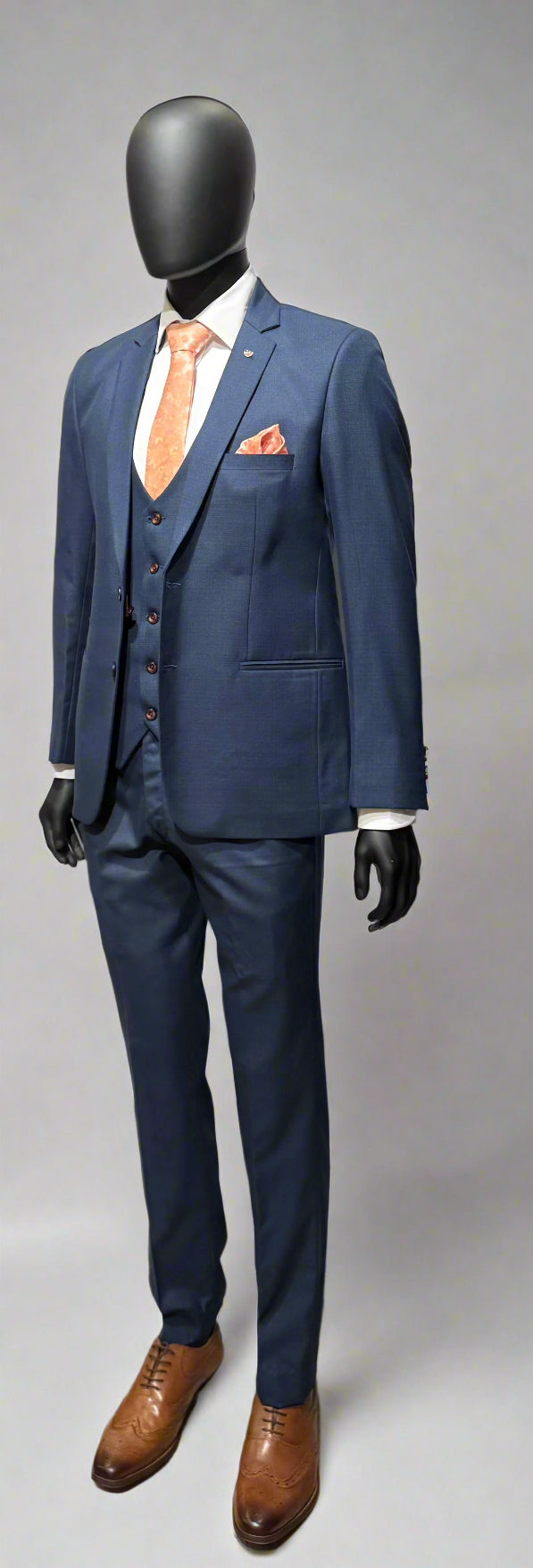 Navy blue suit with a white shirt, orange tie, and brown shoes on a gray background