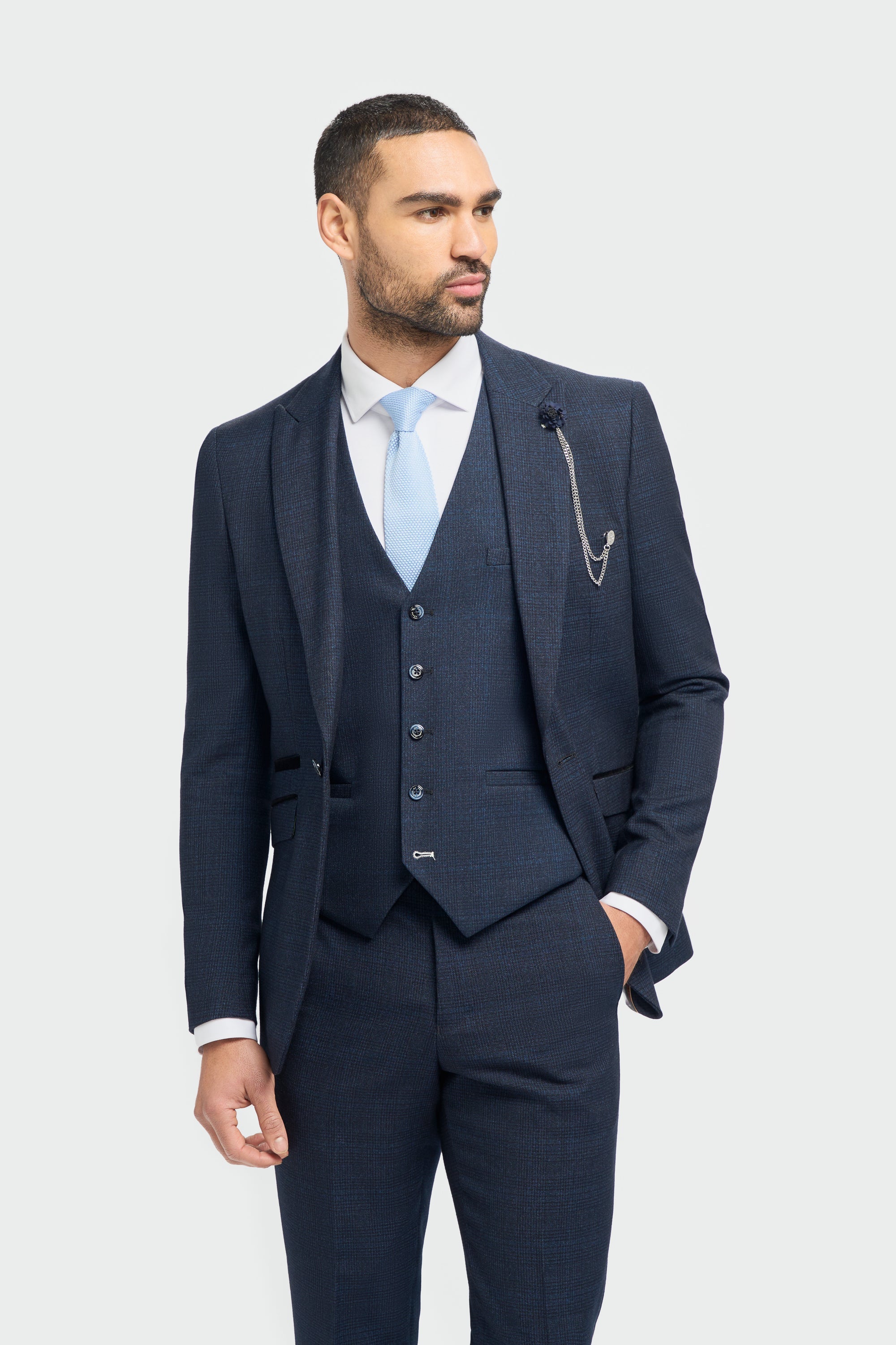 A male model wearing a House Of Cavani Caridi Navy Three Piece Suit with a deep navy color, tailored fit, and a regular length. The model is also wearing a white shirt and brown shoes.