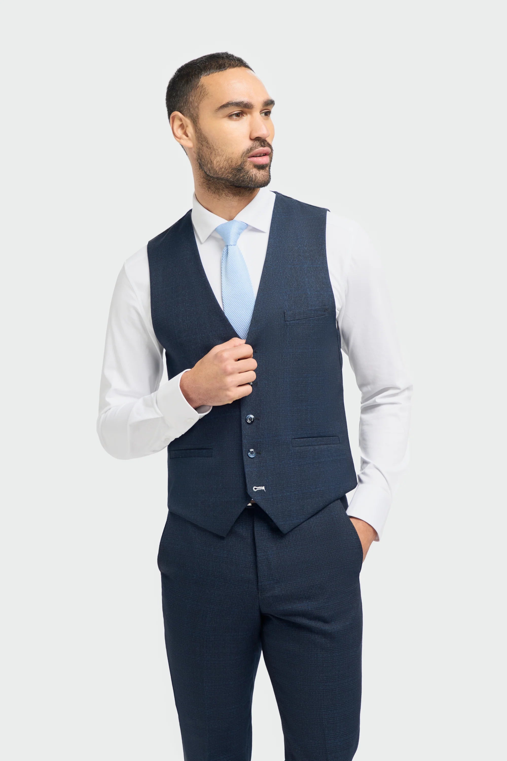 A male model wearing a House Of Cavani Caridi Navy Three Piece Suit with a deep navy color, tailored fit, and a regular length. The model is also wearing a white shirt and brown shoes.