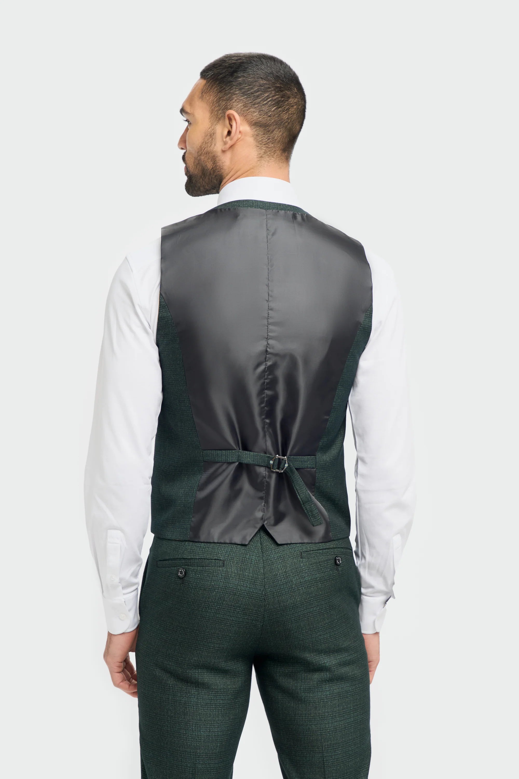 Man wearing a dark green vest and green pants on a plain background