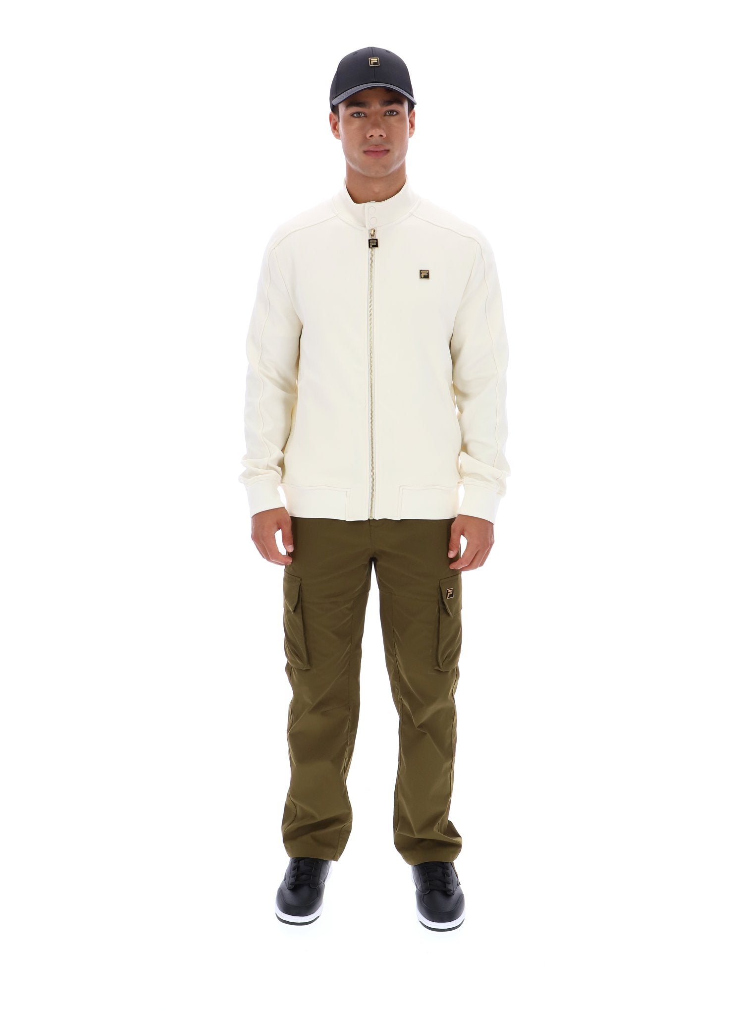 Person wearing a cream jacket, green pants, and a black cap on a white background