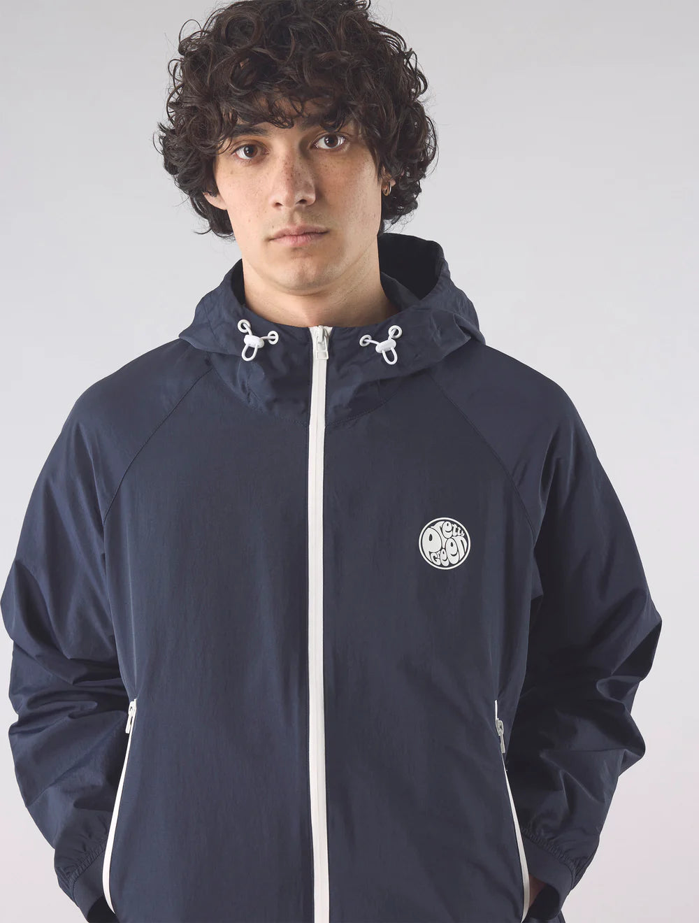 Person wearing a navy blue jacket with a white logo on a light gray background