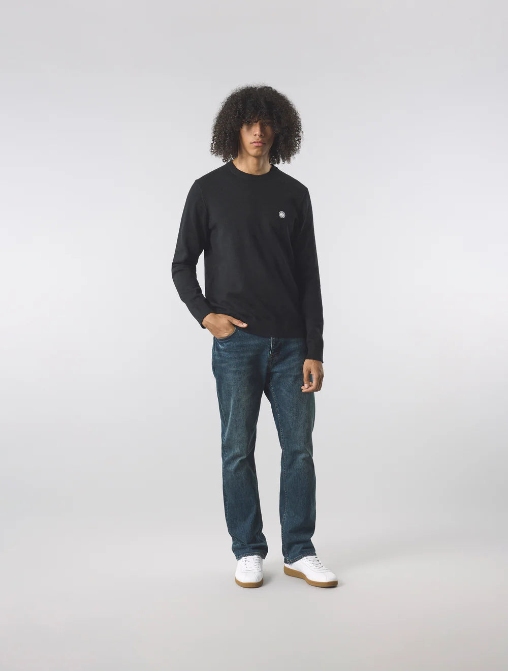 Person wearing a black long-sleeve shirt and blue jeans on a white background