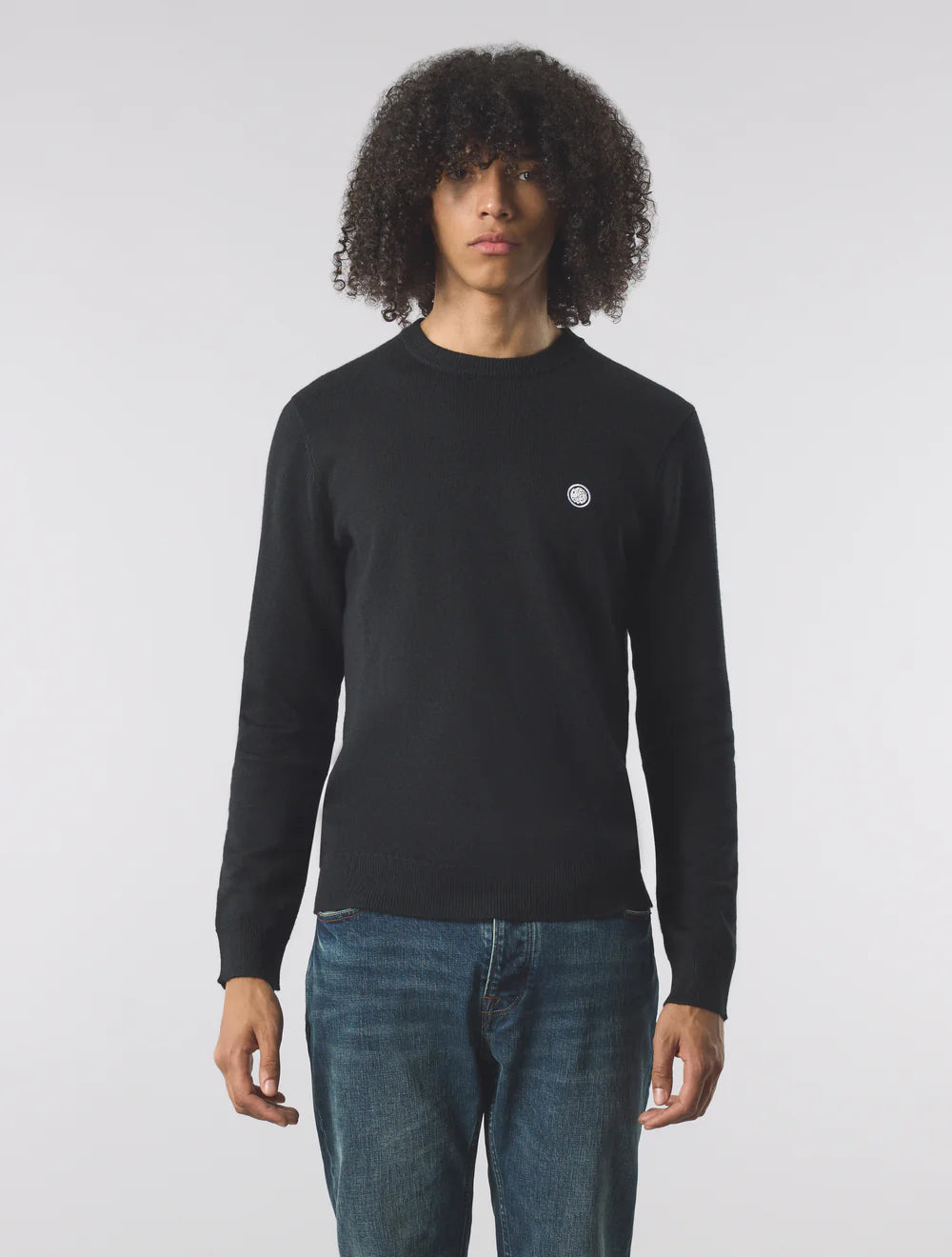 Person wearing a black sweater with a small logo on a white background