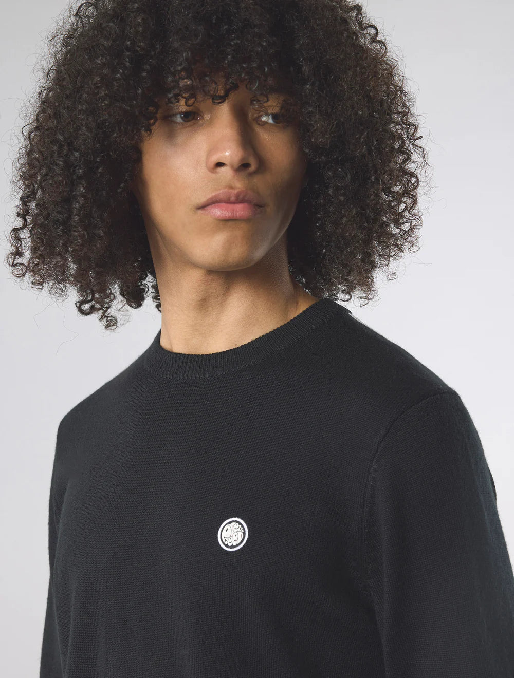 Person wearing a black sweater with a small logo on a plain background
