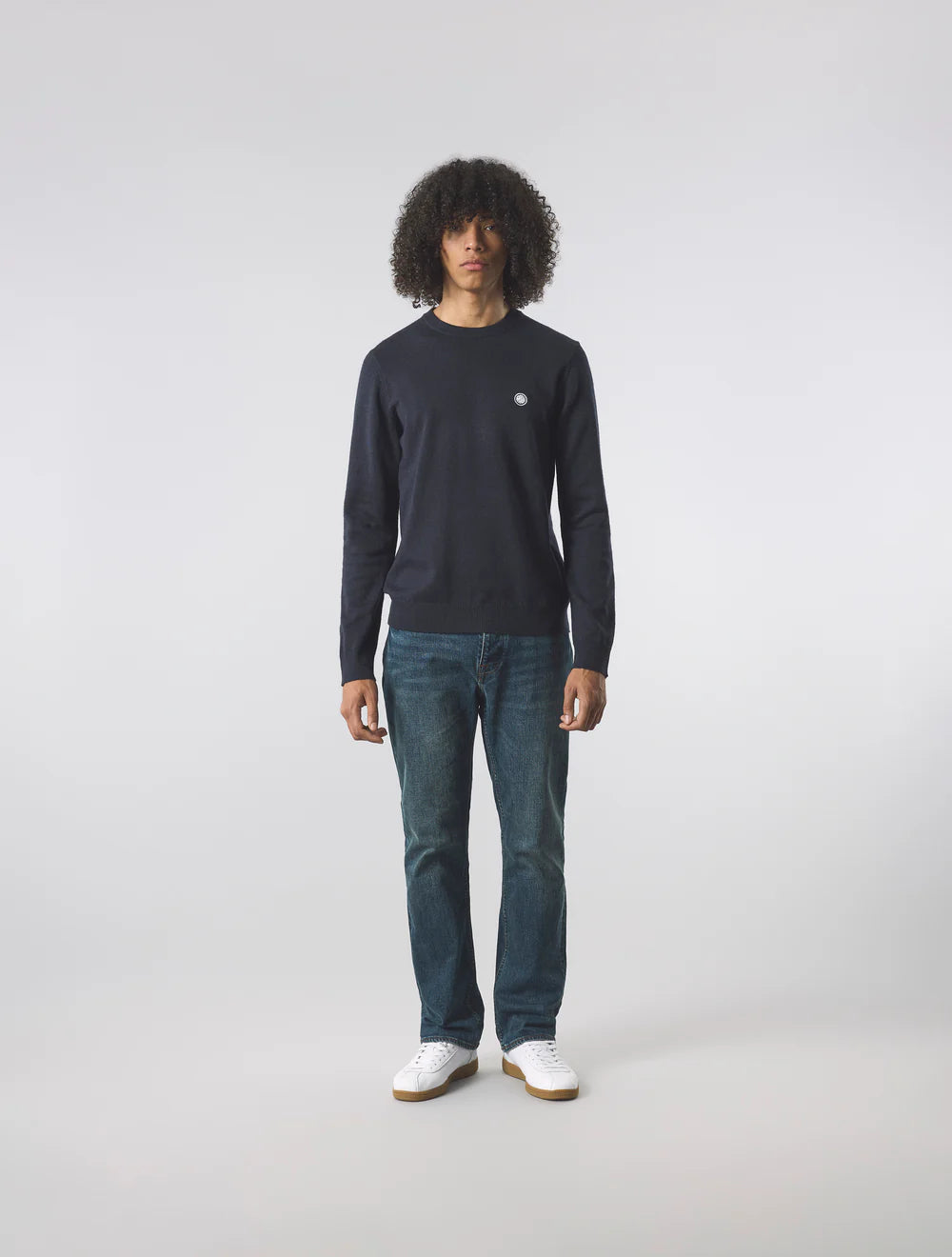 Person wearing a black long-sleeve shirt and blue jeans on a white background