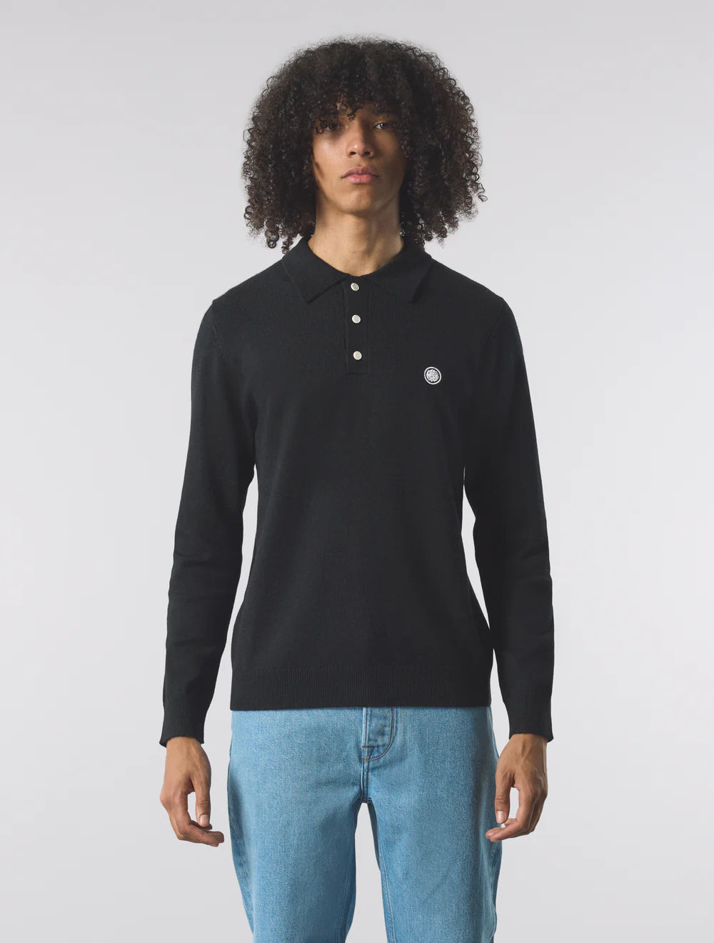 Person wearing a black long-sleeve polo shirt with a logo on a plain background