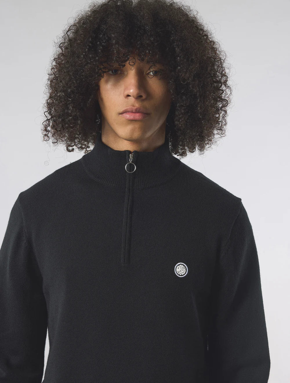 Person wearing a black quarter-zip sweatshirt with a logo on a white background