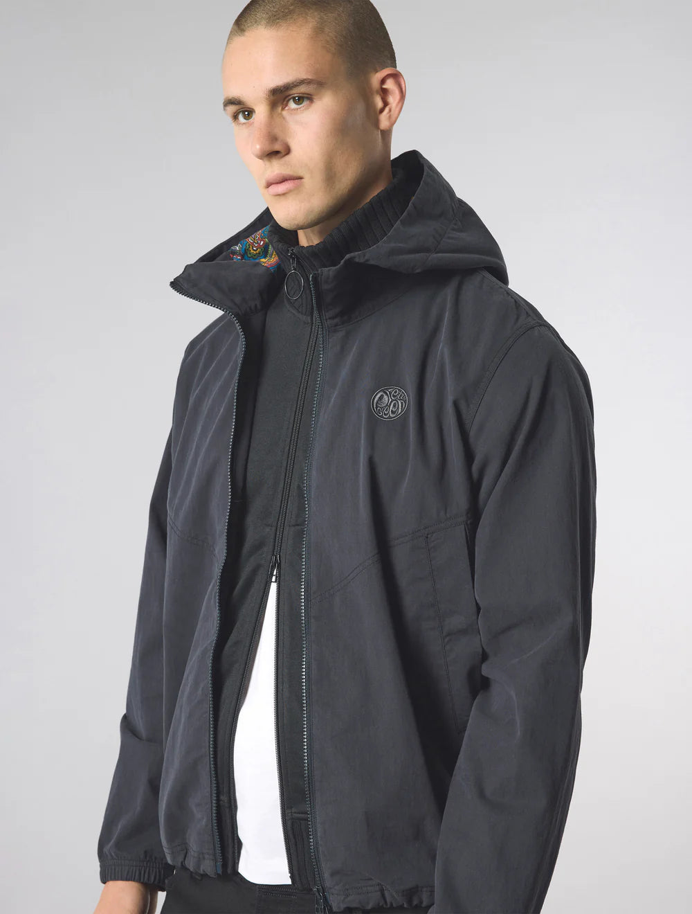 Man wearing a black jacket with a hood on a plain background