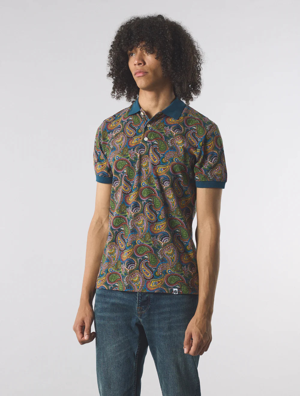 Man wearing a patterned polo shirt and jeans on a white background