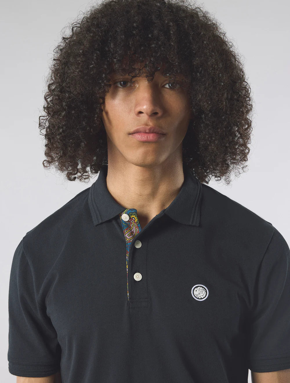 Person wearing a black polo shirt with a visible brand logo on a plain background