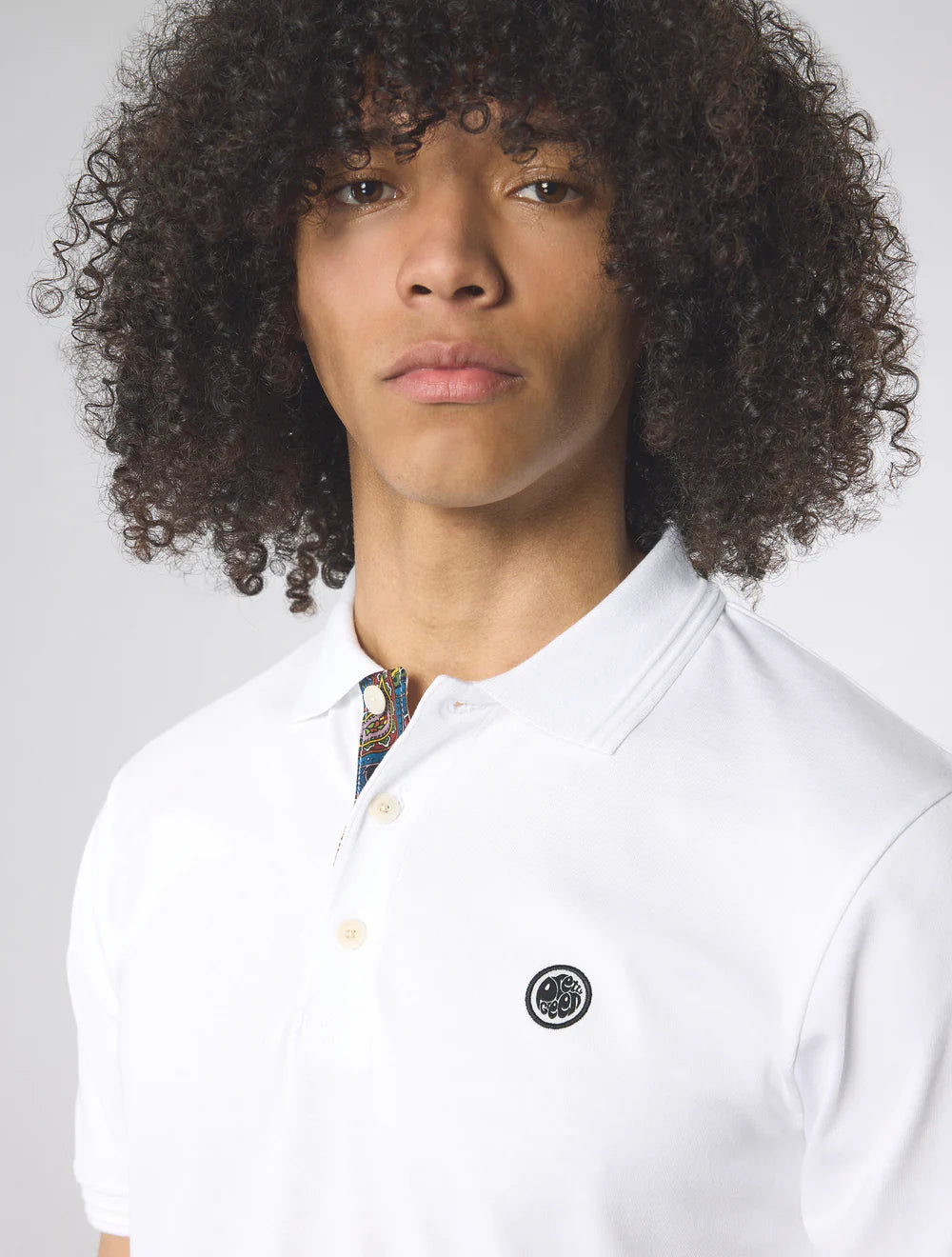 Person wearing a white polo shirt with a small logo on a plain background