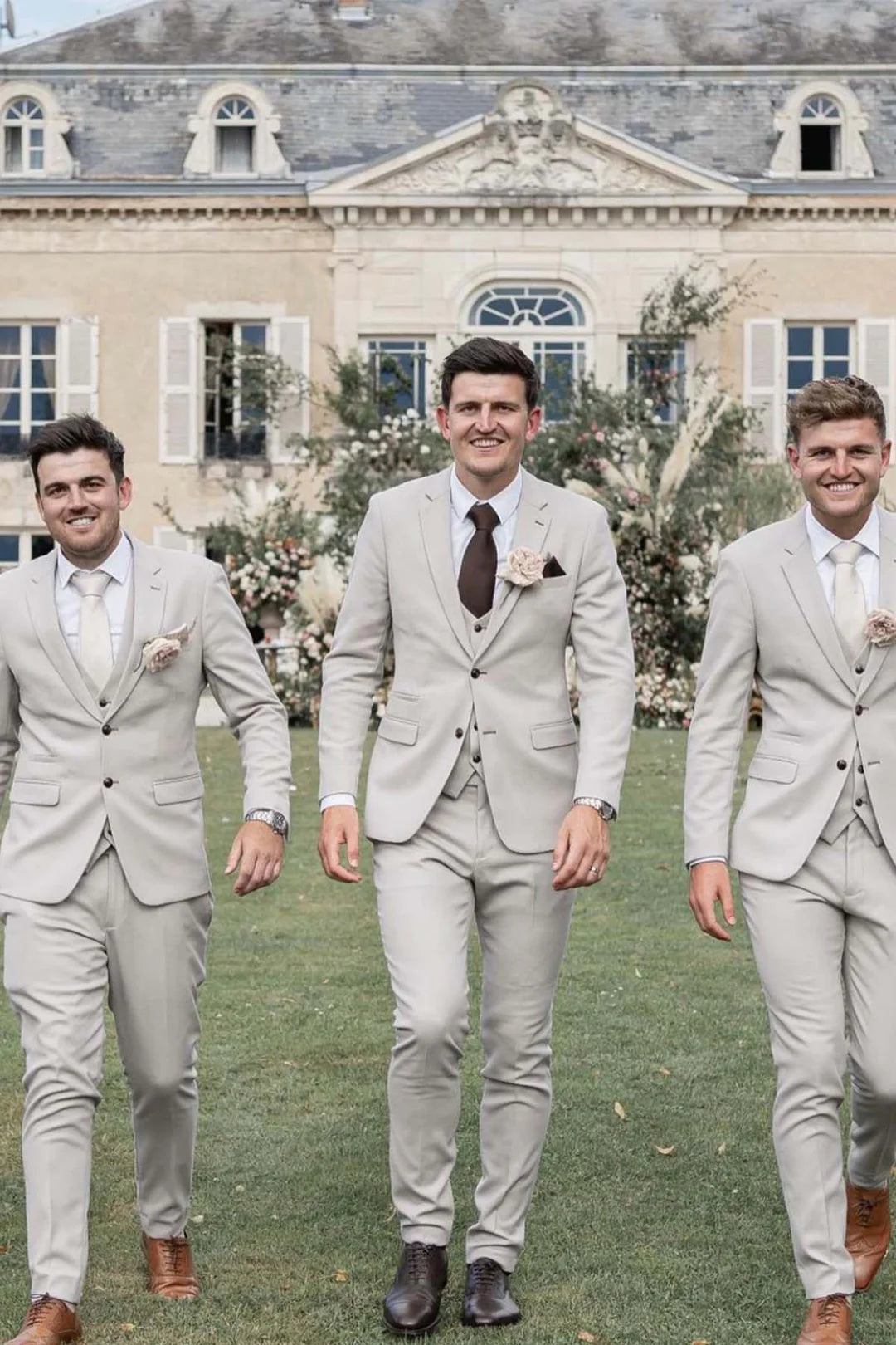 Three men in a garden wearing an beige three-piece suits with notch lapels and matching pocket squares.