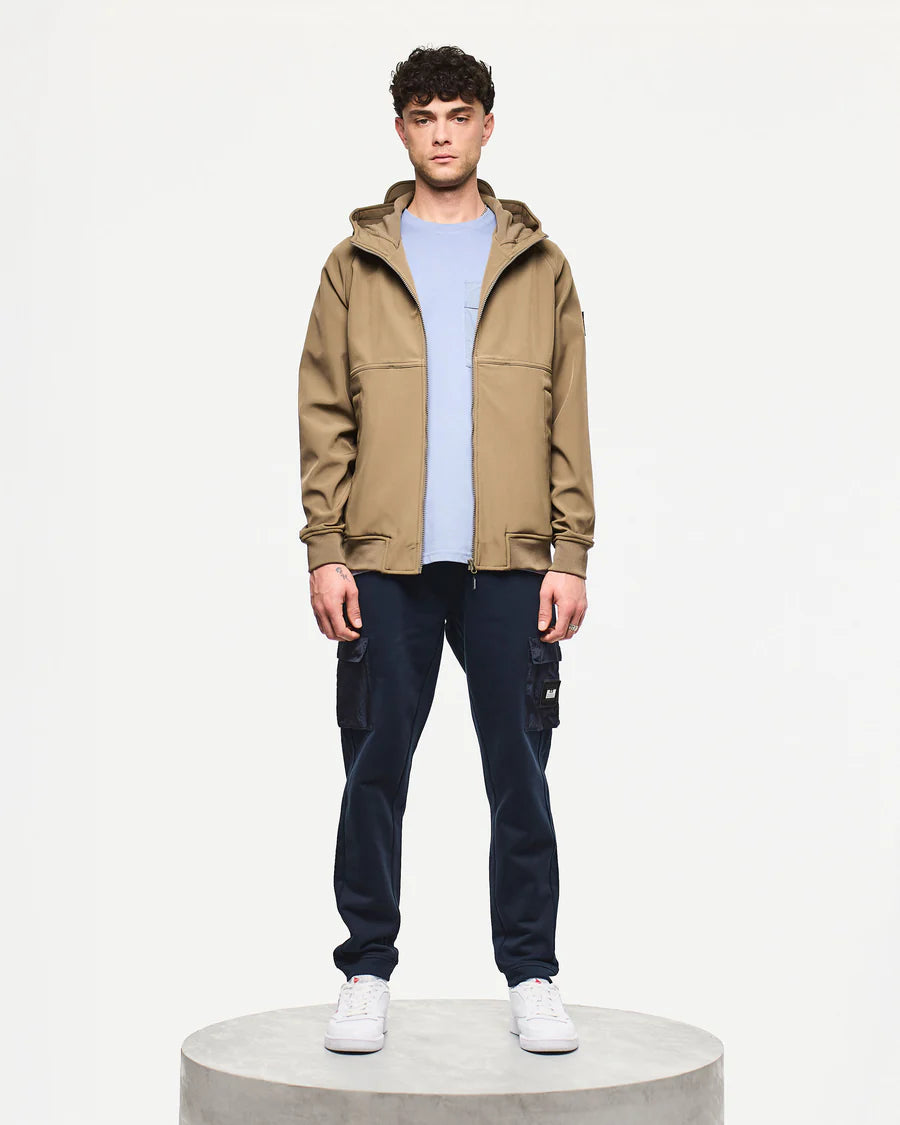 Man wearing a beige jacket, light blue shirt, dark pants, and white sneakers on a white background