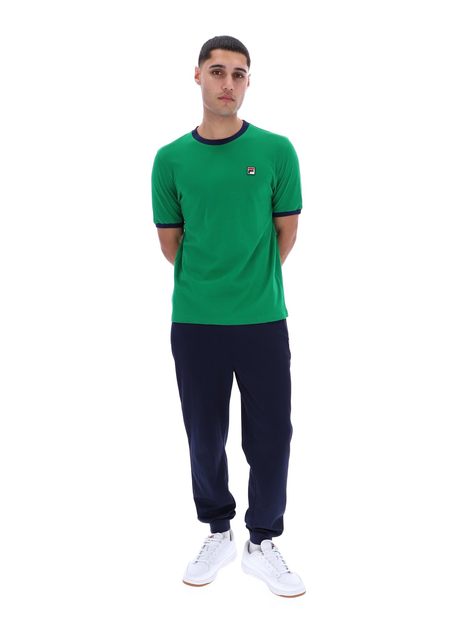Man wearing a green t-shirt with a logo and dark pants on a white background