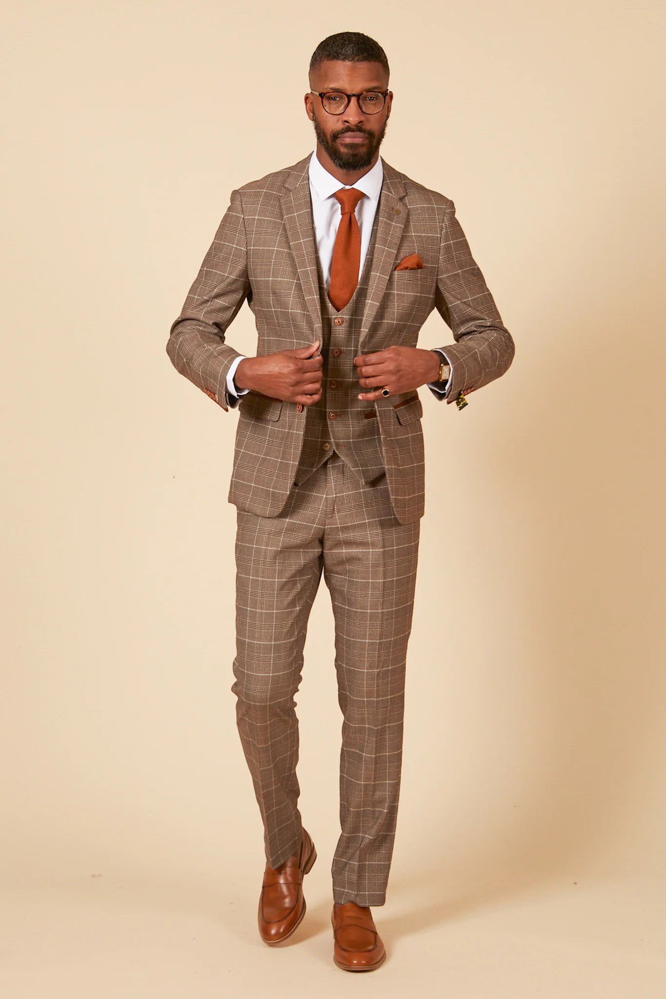 Man wearing a brown checkered suit with a white shirt and orange tie on a beige background
