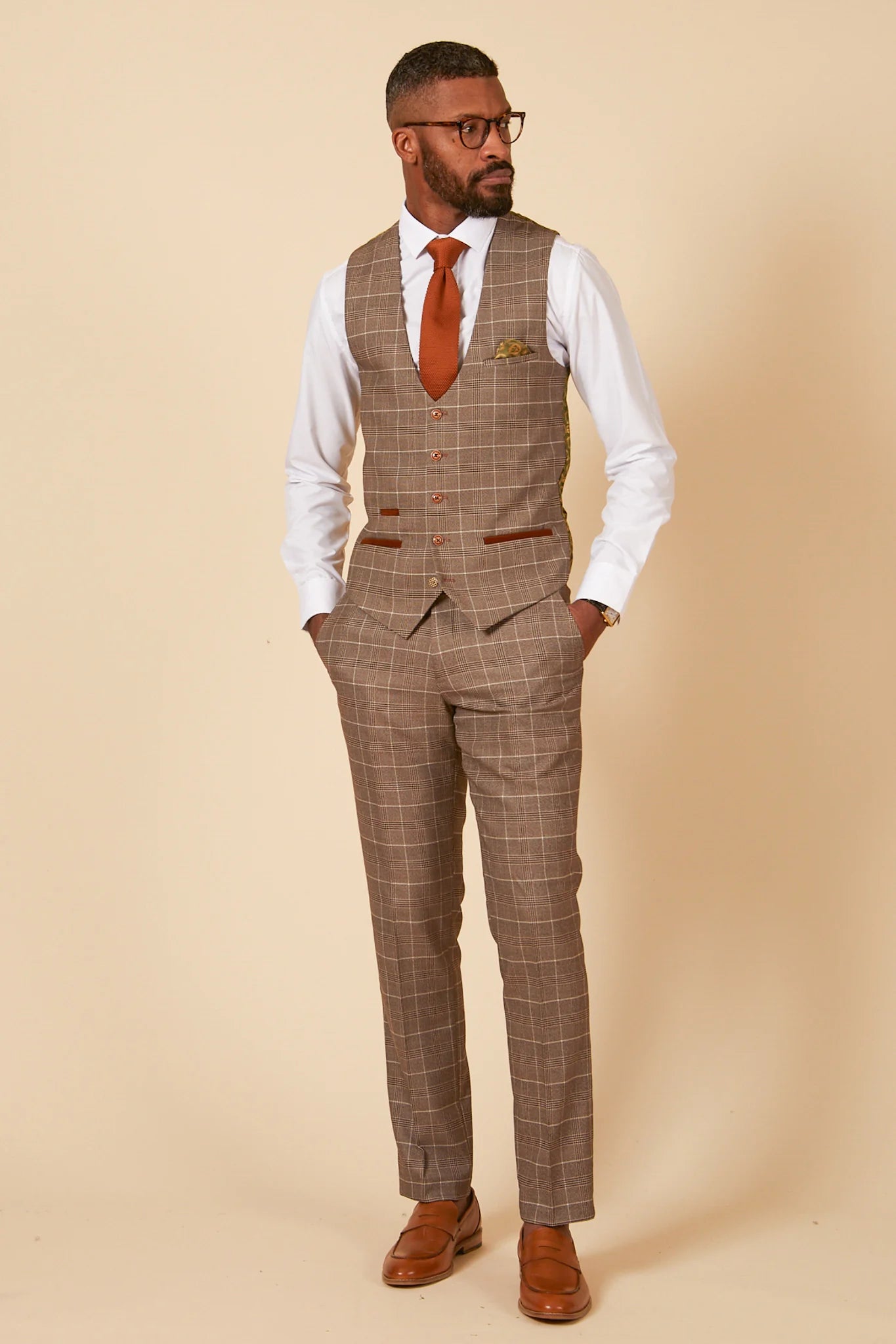 Man wearing a brown checkered suit with a white shirt and orange tie on a beige background