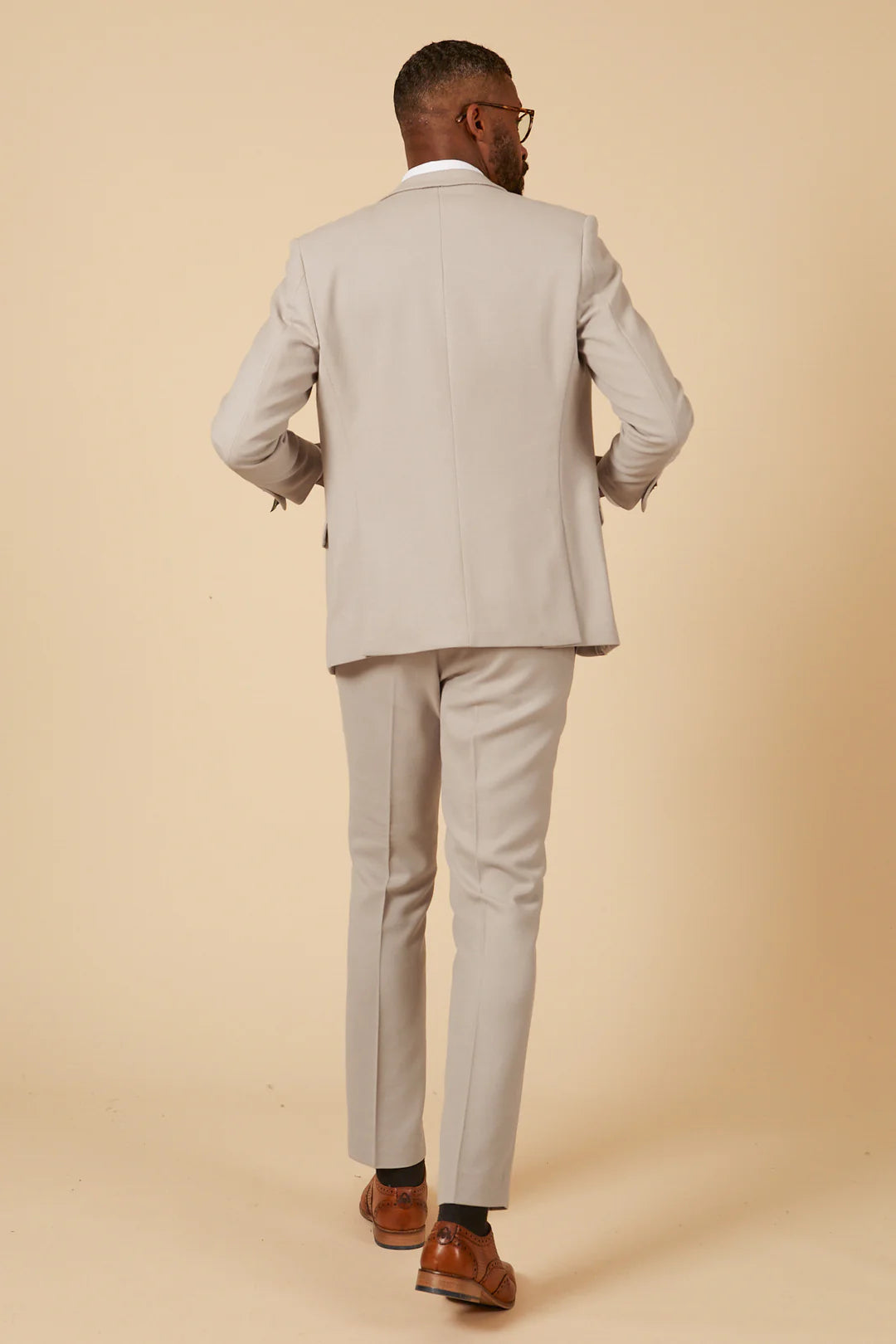 A man wearing a beige three piece suit with a blue tie and brown shoes.