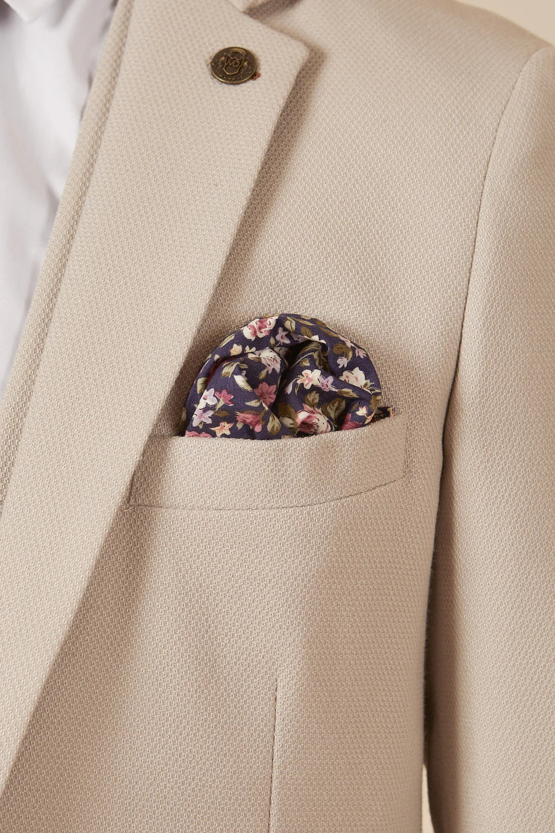 A man wearing a beige three piece suit with a blue tie and brown shoes.