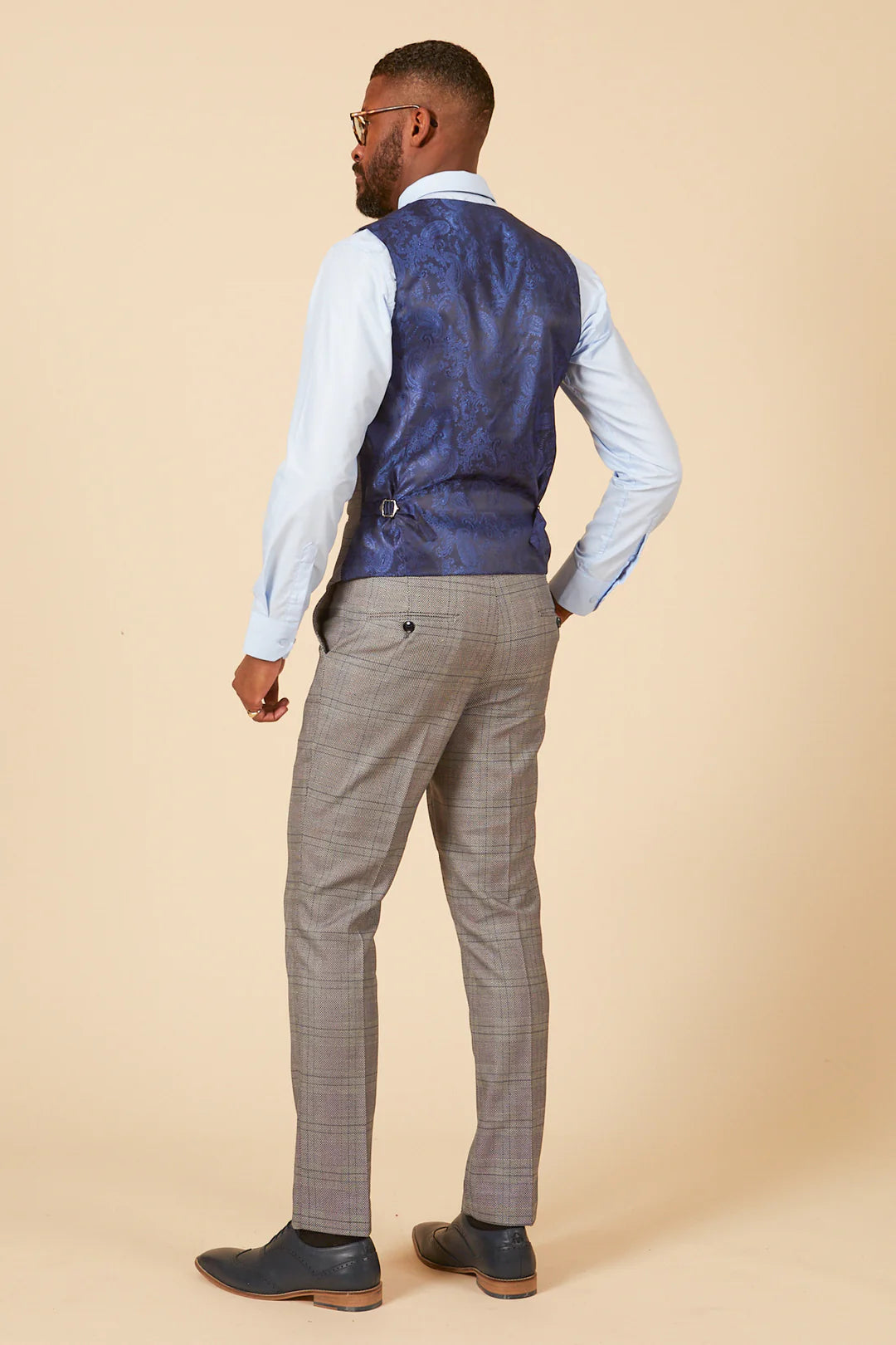 Man wearing a blue vest and gray pants against a beige background