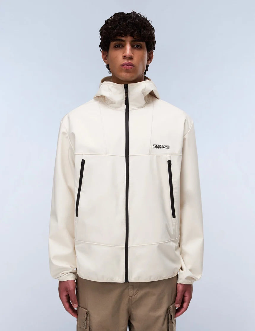 A model wearing a cream-colored hooded jacket with black zippers and a small black logo on the chest, paired with khaki cargo pants, against a light gray studio background.