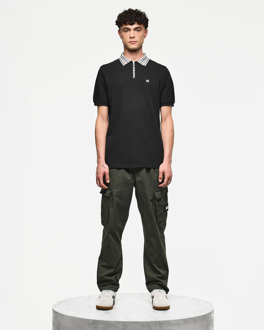 Man wearing a black polo shirt and green cargo pants on a white background