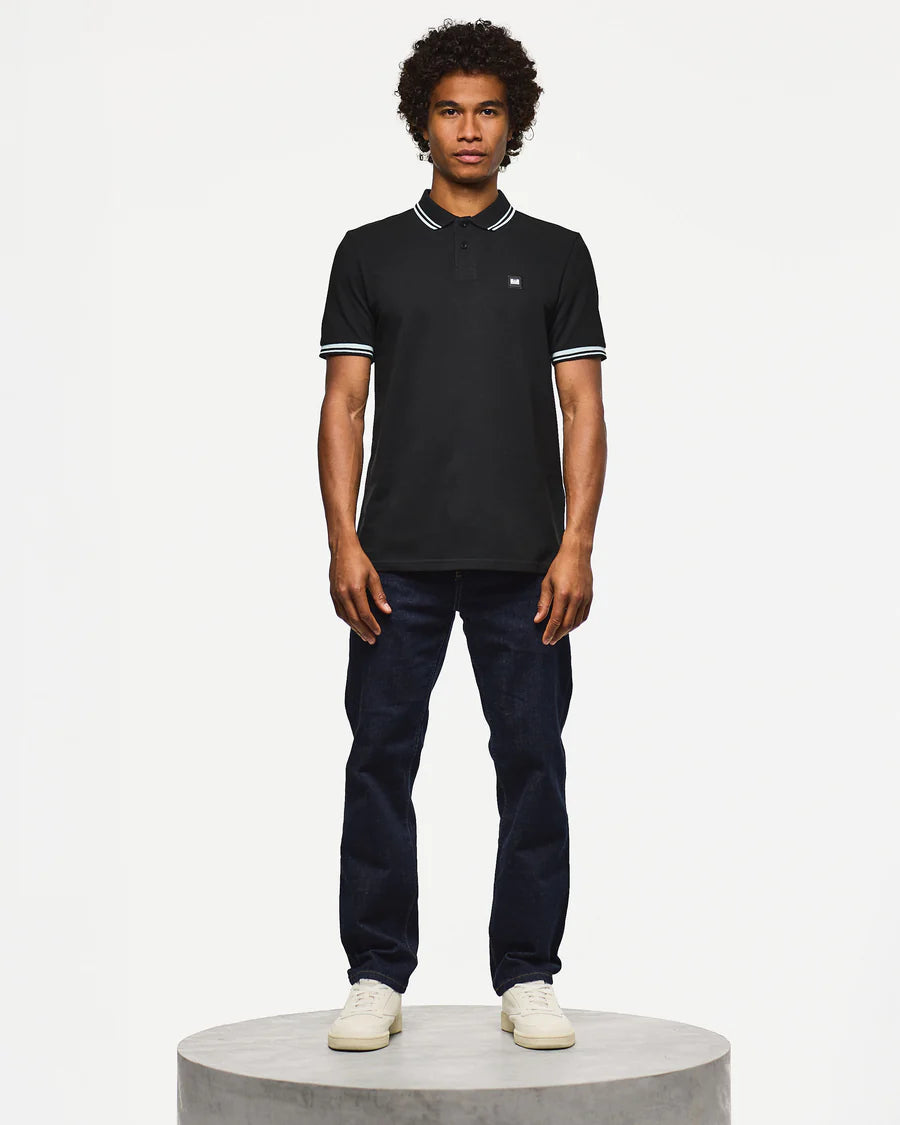 Man wearing a black polo shirt and dark jeans on a white background