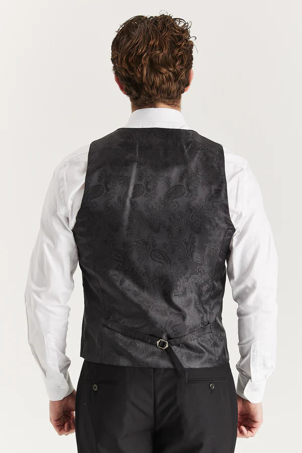 Man wearing a black patterned vest over a white shirt on a light gray background