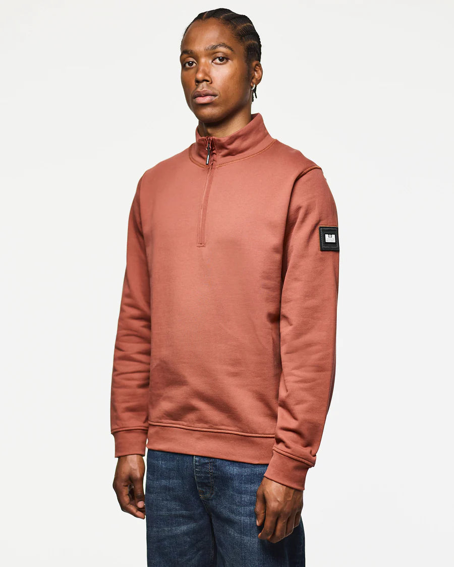 Person wearing a brown sweatshirt with a patch on a white background