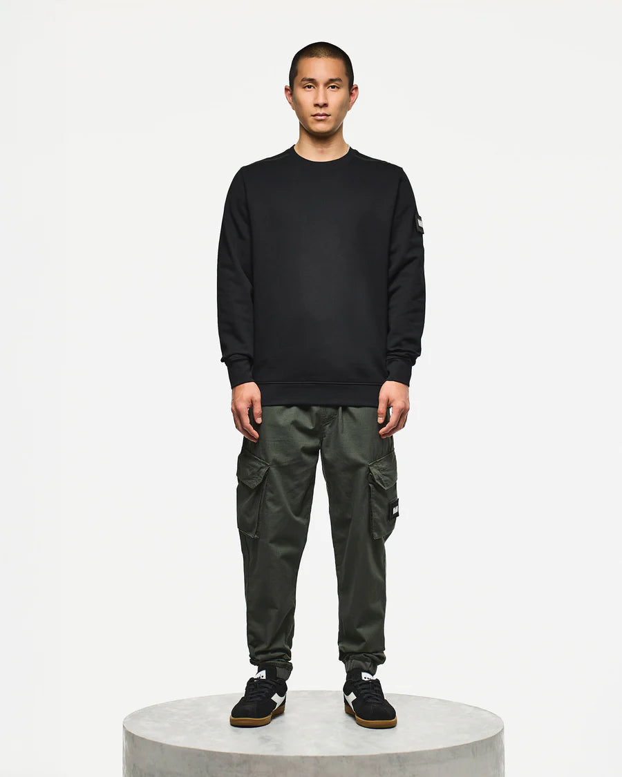 Person wearing a black sweatshirt and green cargo pants on a white background